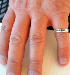 Photo of a person's hand with ring that says "fear not"