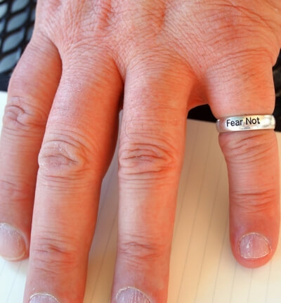 Photo of a person's hand with ring that says "fear not"